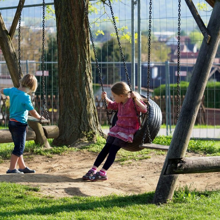 Kinder auf den Schaukeln des Spielplatzes im Garten
